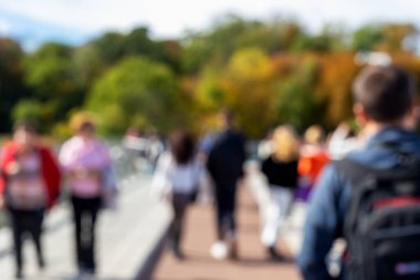 Bulanık arka plan insanları parkta yaya köprüsünde yürüyor, insanlar güneşli bir sonbahar gününün tadını çıkarıyor. Şehir yürüyüşü ve boş zaman kavramı. Yaya köprüsündeki bulanık arkaplan insanları