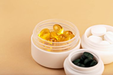 Sarı kapsüller, yeşil tabletler ve bej arka planda açık plastik kaplarda beyaz haplar. Sağlık ve sağlık ürünleri veya destek ambalajı kavramı. Vitaminler ve takviyeler açık kavanozlarda