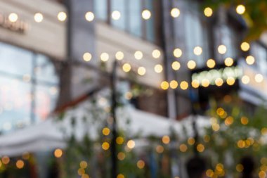 Şehir caddesinde parlayan sicim ışıklarının bulanık arkaplanı, yanan binalar ve ağaçlar. Şenlikli şehir havası. Şehir caddesinde bulanık sicim ışıkları