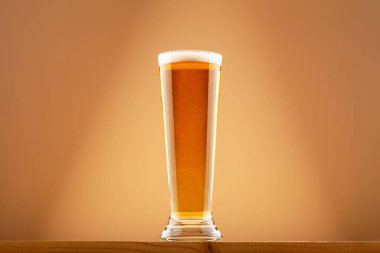 Bir bardak kehribar birası, yumuşak köpüklü, ahşap tahtada, arka planda sıcak bir eğim var. Bira serinletici, altın bira ve sıradan içki anı kavramı. Bira en az rahat atmosferde yakalanır.
