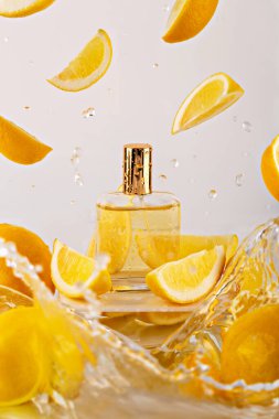 Limon dilimleriyle çevrili taze parfüm şişesi ve beyaz arka planda su sıçramaları. Turunçgil kokusunu, enerjiyi ve yaz tazeliğini ürün reklamcılığında kabul edin. Limon aromalı parfüm