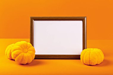 Cadılar Bayramı. Modelleme. Canlı turuncu arka plan, dekoratif sarı balkabaklarıyla çevrili boş ahşap bir çerçeve içeriyor. Cadılar Bayramı kutlamaları ve mevsimsel dekorasyon için mükemmel bir şenlik ortamı yaratıyor.