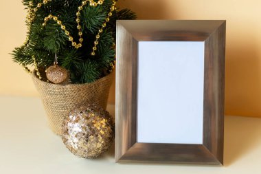 Modelleme. Noel zamanı. Altın süslerle süslenmiş Noel ağacının yanına yerleştirilmiş dekoratif çerçeve, bayram kutlamaları için mükemmel bir ortam yaratıyor.