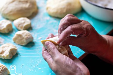 Turta pişiriyorum. Yetenekli yaşlı fırıncının elleri, un ve diğer hamur parçalarıyla çevrili turkuaz tezgahtaki ev yapımı turşular için ustalıkla hamur şekillendiriyor ve sıcak ve davetkar bir ortam yaratıyor.