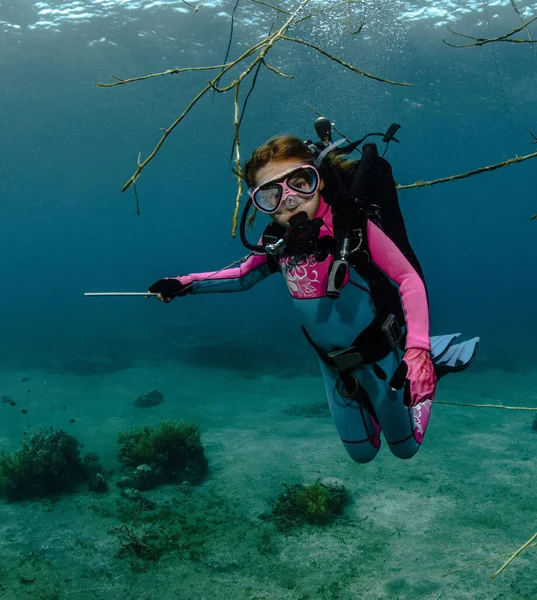 A child diver shows with his hand where to move, diving underwater in scuba against the backdrop of a coral reef in the ocean in the rays of sunlight. Diving training. Scuba diving in the tropical sea