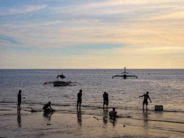 Gün batımında deniz manzarası. Balıkçıların siluetleri güzel bir deniz ufkunun arka planında durgun pastel renklerle
