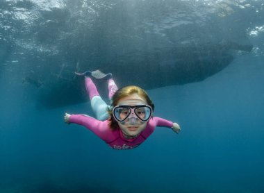 Mavi okyanus suyuna dalan küçük bir kızın sualtı portresi güneş ışığının altında dalgıç maskesi takmış fotoğrafçıya bakıyordu. Dalış merkezi, dalış yapan çocuklar