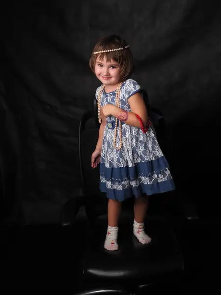 Siyah arka planda mavi elbiseli, mücevherli küçük bir kızın tam boy portresi.