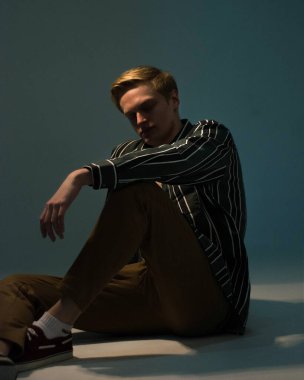 Çizgili gömlekli genç sarışın adam kameraya bakıyor.