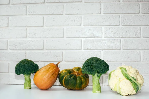 Broccoli, cauliflower, pumpkins on a white table with a white brick background. Front view