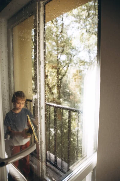 A boy washes windows at home using a cordless window cleaner. Front view, selective focus