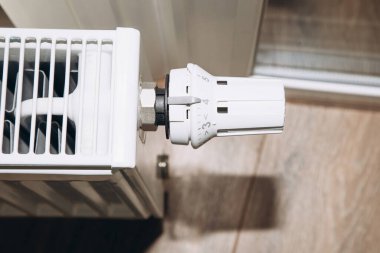 Beyaz metal batarya, panoramik pencerenin yanında, termostatı yakın çekimde. Daire ısıtma, üst görünüm