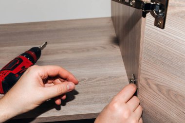 Bir dolabı monte ederken kırmızı bir tornavidayla erkek ellerine yakın çekim. Ön görünüm, seçici odak