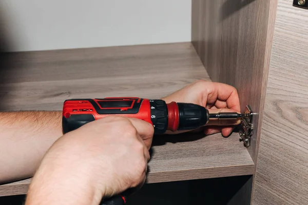 stock image Close-up of male hands with a red screwdriver while assembling a cabinet. Front view, selective focus