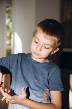Mavi tişörtlü bir çocuk mutfakta simit yiyor, simit ve kurabiye ile yüzünü buruşturuyor. Ön görünüm
