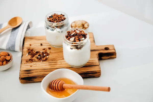 stock image Yoghurts in glass jars with blueberries, raspberries and chia seeds and granola on a wooden plank on a white background. The concept of healthy eating. Front view