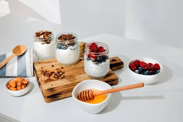 キッチンタオルで白い背景にグラノーラ チョコレート 蜂蜜とナッツとガラス瓶のヨーグルト 健康的な食事の概念 正面図 — ストック写真