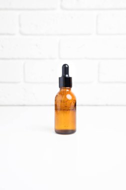 Bir kehribar şişesi, beyaz bir masada pipetli, kendi kendine bakım kozmetik ürünleri. Ön görünüm