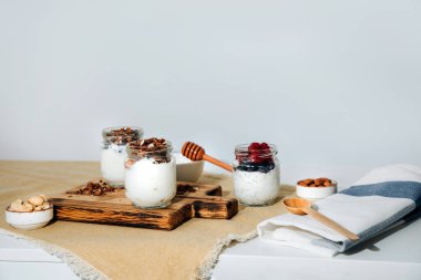 Yaban mersini, ahududu ve chia tohumlarıyla dolu cam kavanozlarda yoğurtlar ve beyaz bir zemin üzerinde tahtadan yapılmış tahıl gevreği. Sağlıklı beslenme kavramı. Ön görünüm