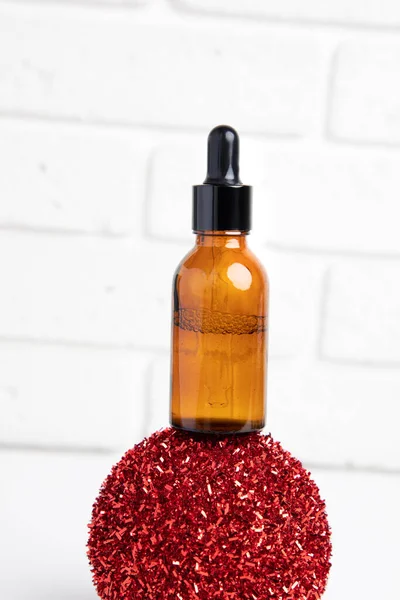 One amber bottle with a pipette on a red shiny ball on a white background, selfcare cosmetic products. Front view