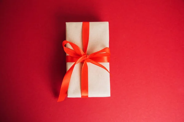 Egy Ajándék Barna Papírba Csomagolva Piros Szalaggal Piros Háttérrel Karácsonyi — Stock Fotó