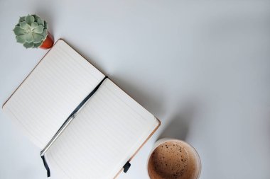 Kırtasiyeli beyaz bir masada, eko bardakta köpüklü kahve. Düz yatıyordu