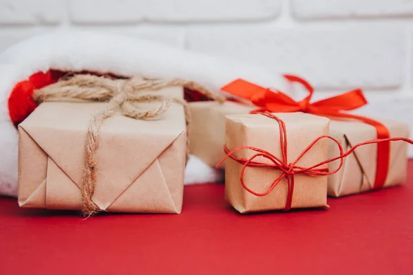 Ajándékok Barna Csomagolásban Karácsonyi Sapkában Piros Háttérrel Boldog Karácsonyt Előnézet — Stock Fotó