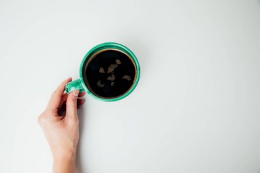 Bir kadının eli, beyaz bir masanın üzerinde siyah kahve olan yeşil bir kupayı tutar. Düz yat, boşluğu kopyala