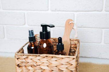 Banyo için kozmetik ürünlerle dolu kehribar şişeleri ve beyaz arka planda saman bir sepetin içinde. Ön görünüm