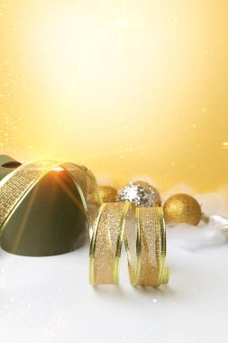 Yeni yıl ve Noel geçmişi. Altın dekoratif kurdele ve yeşil yuvarlak hediye. Sarı arka planda, melek saçlı. Ön görünüm