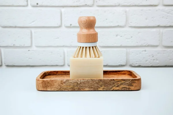 Eco friendly products. Washing brush and natural soap on a wooden tray on a white table. Front view