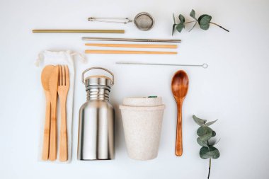 Çevre dostu ürünler seti, sıfır atık konsepti. Su için teneke kutu ve beyaz arka planda tekstil torbalarının üzerindeki bambu çatal bıçak takımı. Düz yatıyordu