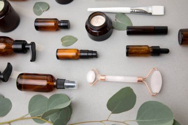 Amber bottles with facial cosmetics with a branch of eucalyptus on the gray concrete background. Top view