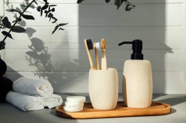 Stone bathroom accessories. Soap dispenser and a glass with wooden tooth counts on a light background with eucalyptus branches. Front view