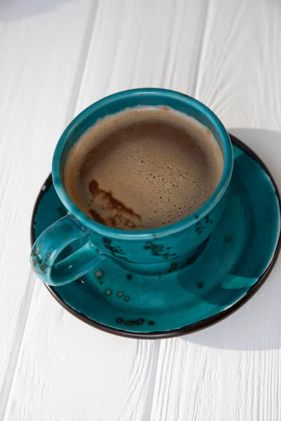 Blue mug with coffee, cappuccino on a white wooden background. Top view, close-up