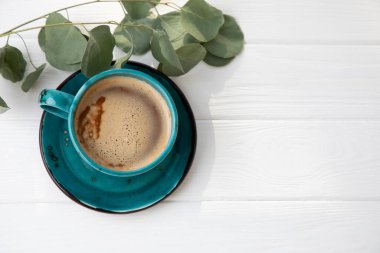 Blue mug with coffee, cappuccino on a white wooden background with eucalyptus branch. Top view, close-up