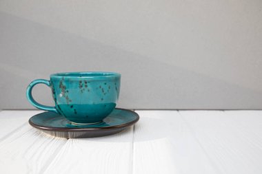 Blue mug with coffee, cappuccino, tea on a white wooden table with shadows. Front view, close-up