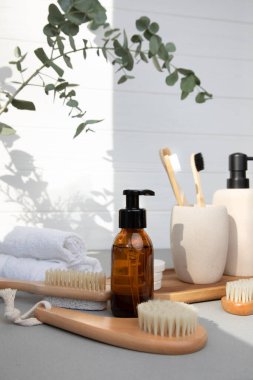 Stone bathroom accessories. Soap dispenser and a glass with wooden tooth counts on a light background with eucalyptus branches. Front view