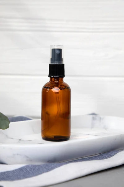 Amber spray bottle with facial cosmetics on a tray with a branch of eucalyptus on the gray wooden background, facial tonec. Front view