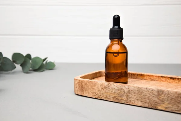 Amber bottle with facial cosmetics on a tray with a branch of eucalyptus on the grey-white background, facial serum. Front view