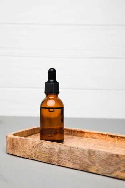Amber bottle with facial cosmetics on a tray on the grey-white background, facial serum. Front view