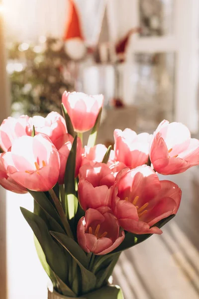 Gently pink bouquet of tulips in a white vase on wooden table. Spring background with a bouquet of flowers. Front view