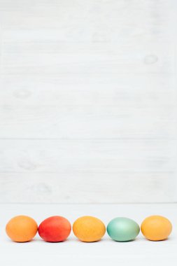Beyaz ahşap arka planda farklı boyutlarda renkli yumurtalar. Paskalya bayramının sembolü. Paskalya geçmişi. Ön görünüm