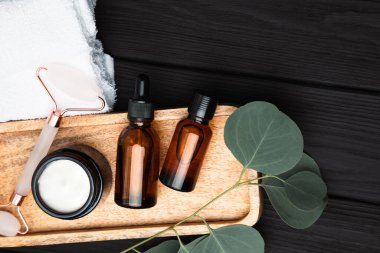 Amber bottles with facial cosmetics with a branch of eucalyptus on the dark wooden background. Top view