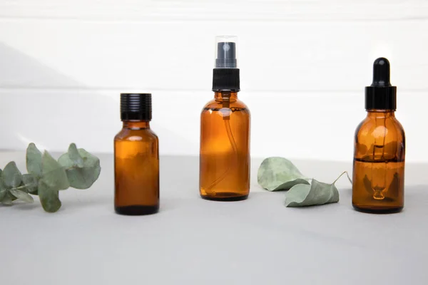 Amber bottles with facial cosmetics with a a eucalyptus leaves on the grey-white background. Front view