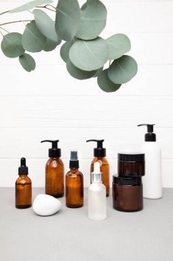 Beyaz ahşap arka planda okaliptüs dalı olan, yüz temizleyici ve serum içeren kehribar şişeleri. Ön görünüm