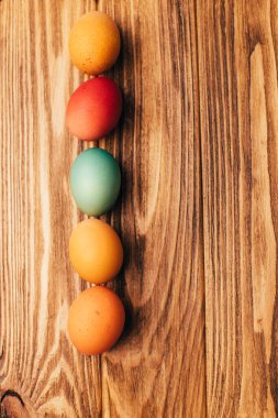 Kahverengi ahşap arka planda farklı boyutlarda renkli yumurtalar. Paskalya bayramının sembolü. Paskalya arkaplanı, üst görünüm