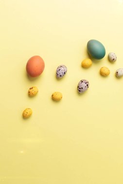 Sarı arka planda farklı boyutlarda renkli yumurtalar. Paskalya bayramının sembolü. Paskalya geçmişi. Düz yatıyordu