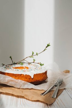 Yuvarlak Paskalya keki, beyaz protein kremi ve beyaz arka planda genç ağaç dallarıyla süslenmiş renkli şekerlerle süslenmiş. Ön görünüm