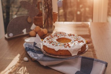 Yuvarlak Paskalya keki, beyaz protein kremi ve mutfaktaki ahşap masaya renkli serpiştirilmiş. Üst görünüm